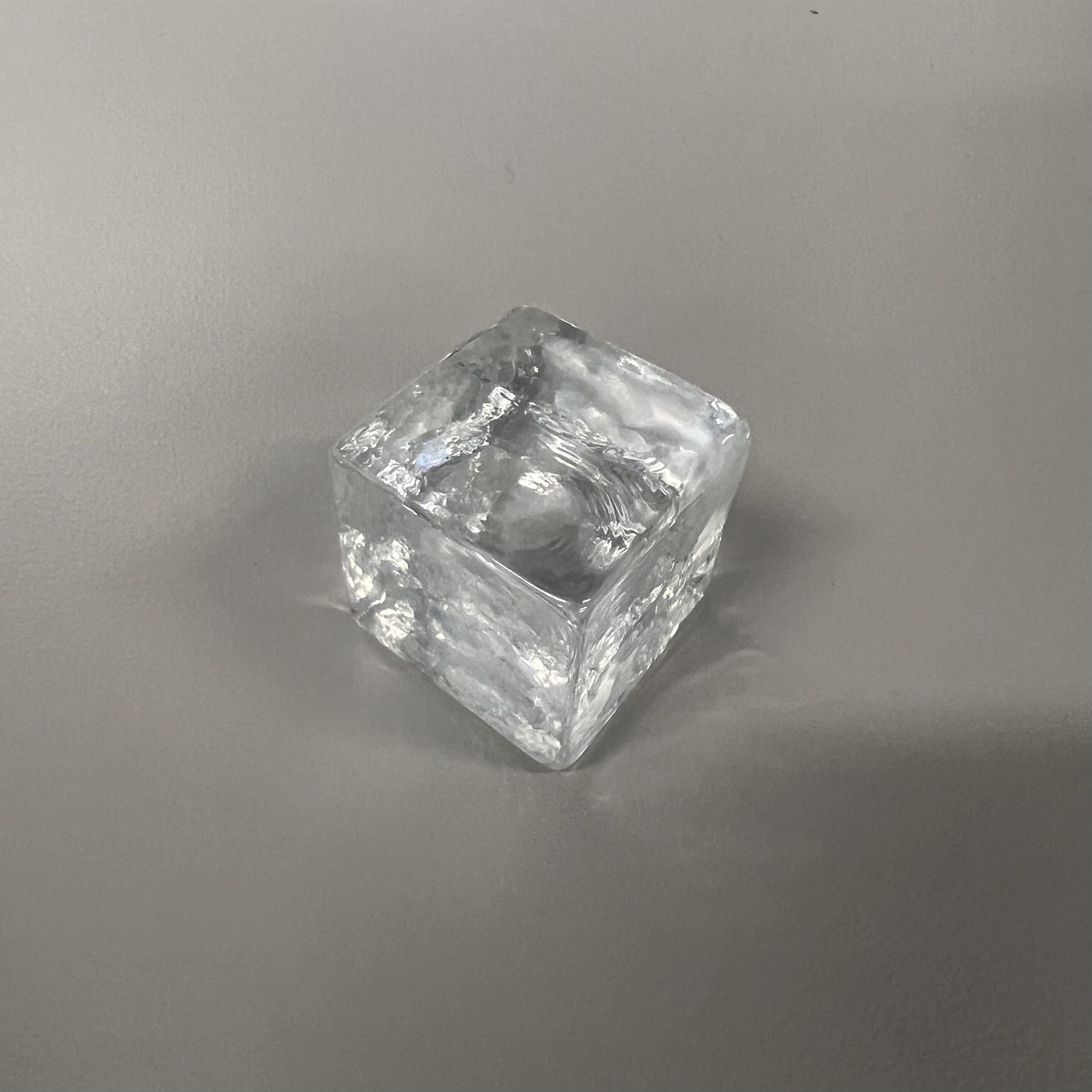 This cube is made out of glass, and it's transparent. It's rigid, smooth, and cool to the touch. The cube is refined, and can be used for windows, containers, and screens.